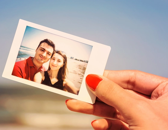 Mano sosteniendo una foto de una pareja en la playa con el mar de fondo